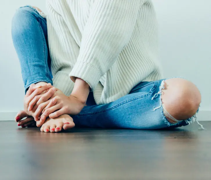 Sitting on Floor With Hands Folded Over Bare Foot